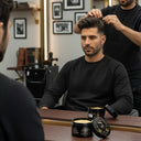 Model getting his hair styled by a barber using SHARK MOLD men's hair styling clay with the product sitting on the counter with its lid open